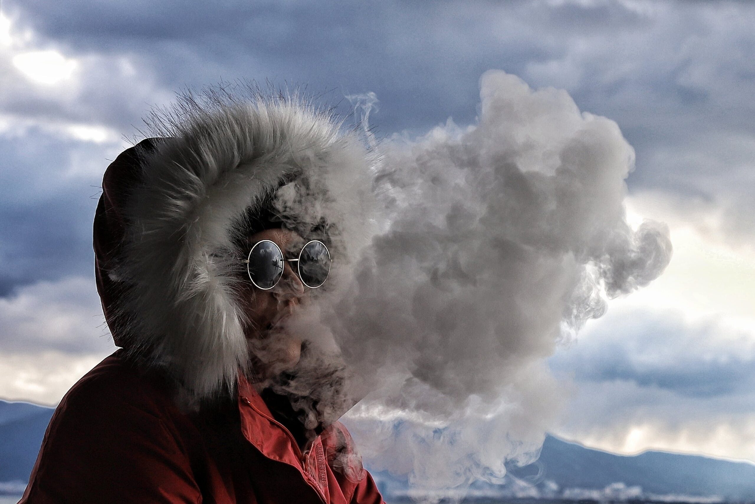 A person in winter attire exhaling smoke, creating a mysterious, moody atmosphere.